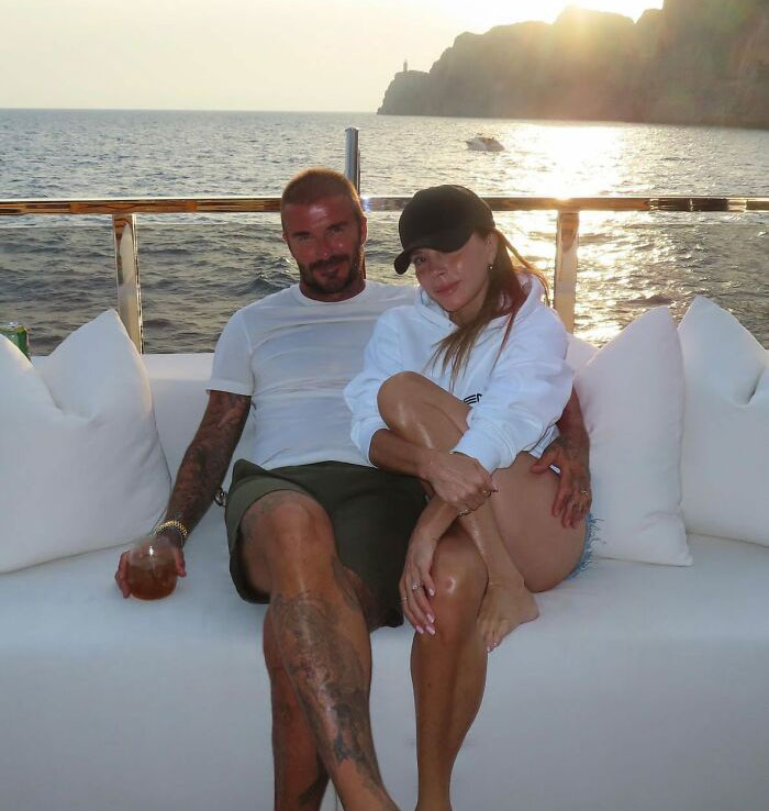 Couple relaxing on a boat at sunset, with ocean and cliffs in the background, amid Brooklyn Beckham family accusations controversy.