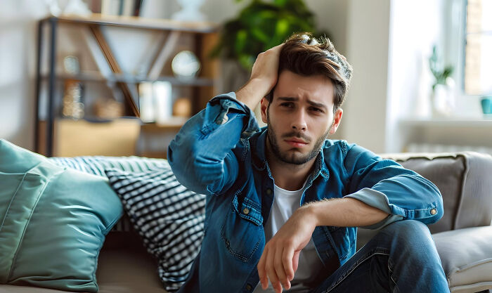 Young man sitting on couch with worried expression, distressed after mom discovered cheating on girlfriend. Young man sitting on couch with worried expression, distressed after mom discovered cheating on girlfriend.