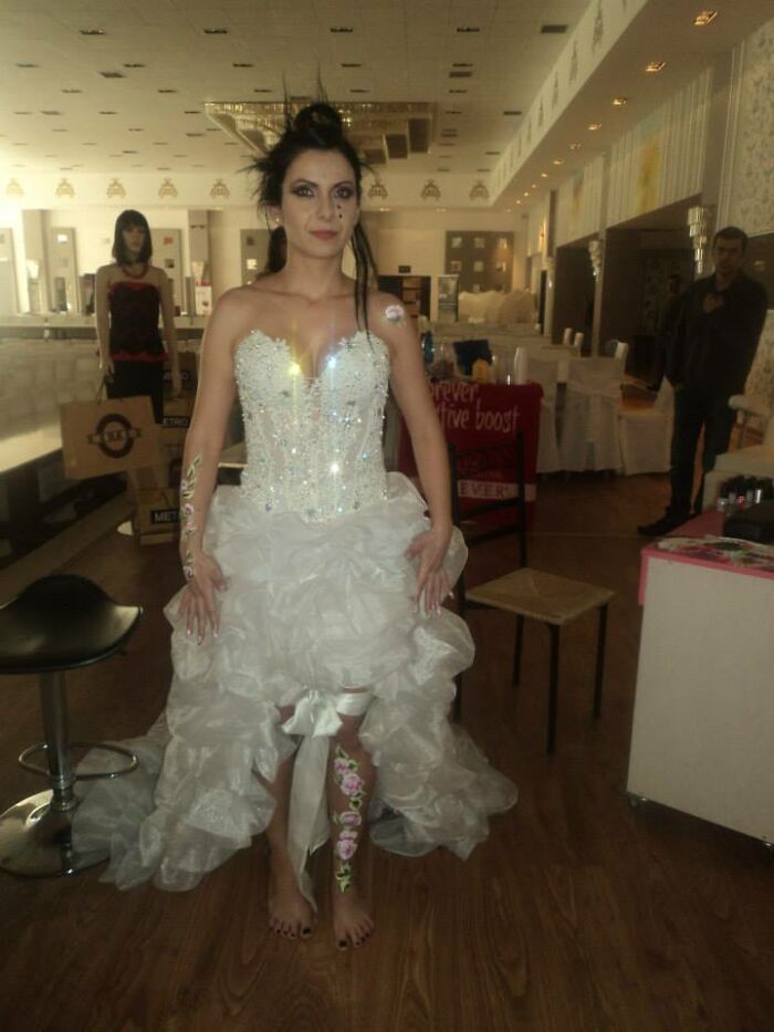 Woman in a sparkling wedding dress with a high-low ruffled skirt and floral body paint in a dimly lit room revealing questionable taste.