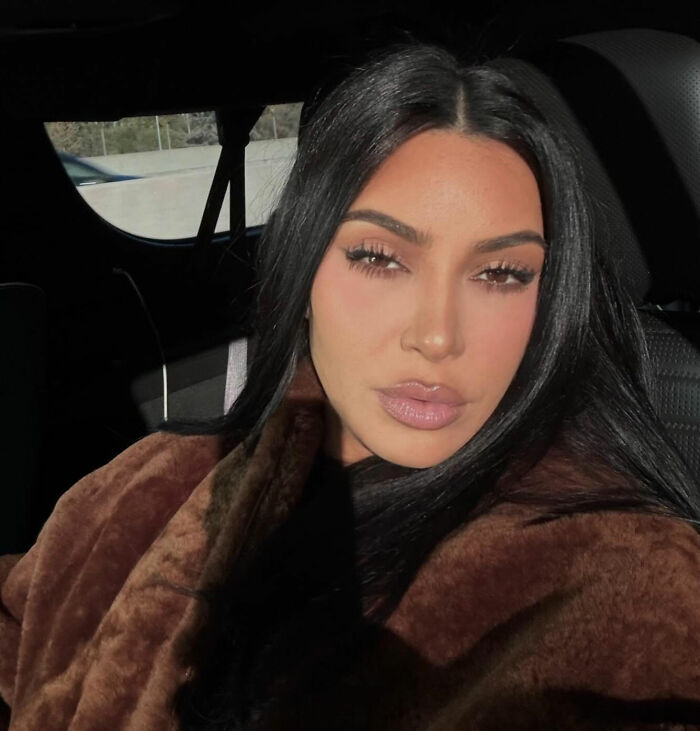 Kim Kardashian in a close-up selfie, wearing a brown coat, sparking suspicion with Taylor Swift comments.