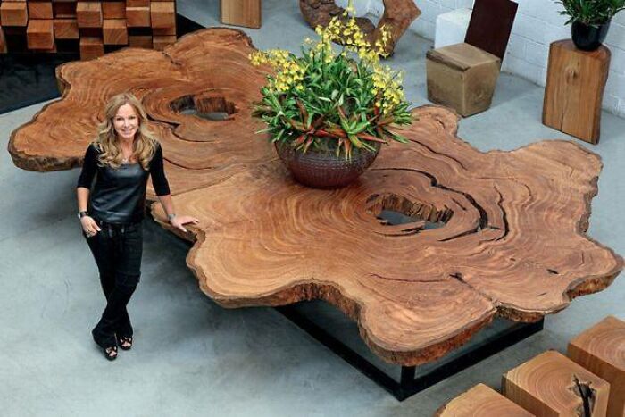 Woman standing beside a large, beautifully crafted woodworking project table made from a natural wood slab with plants.