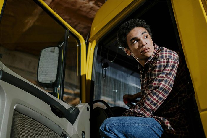 Young man in a plaid shirt sitting in a vehicle, using theatrics for revenge on a workplace bully.