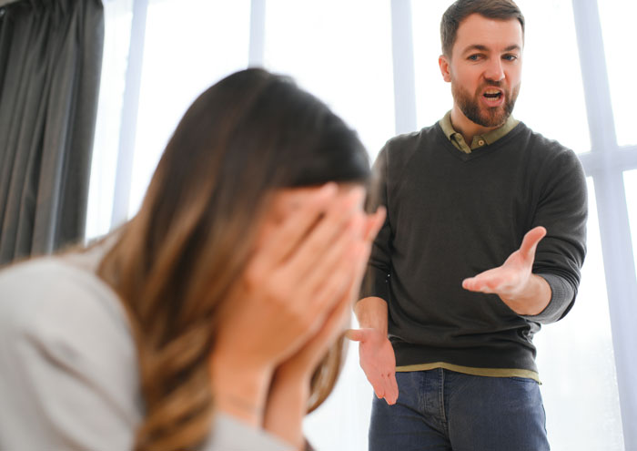 Woman covering her face while boyfriend yells, illustrating red flags in a relationship