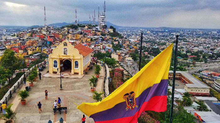 Ecuador hilltop plaza with large national flag overlooking colorful cityscape, illustrating Most Stressful Countries