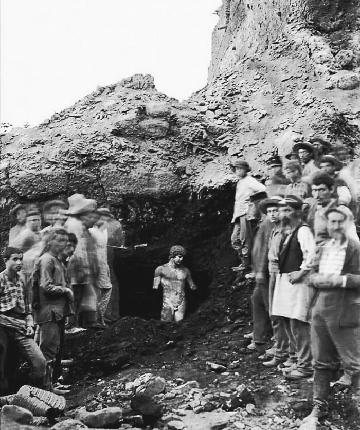 Men gathered at an archaeological site uncovering an ancient statue, capturing a moment in the history of humanity.