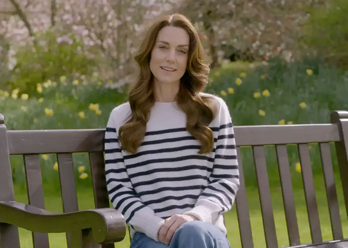 Kate Middleton sitting on a park bench wearing a striped sweater, surrounded by green grass and flowers in spring. Kate Middleton sitting on a park bench wearing a striped sweater, surrounded by green grass and flowers in spring.