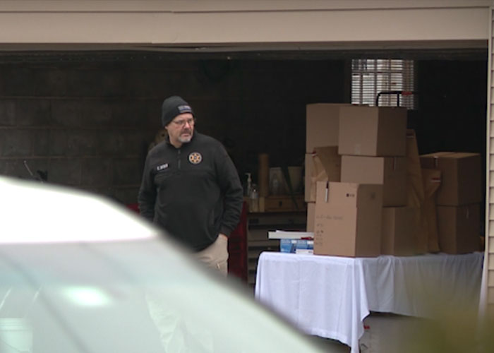 Man in a black jacket and beanie standing near a garage with stacked boxes related to a skull discovery investigation.