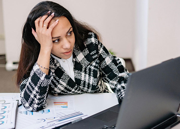 Woman with hand on head looking confused at laptop screen, representing neurodivergent habits misunderstood by others.