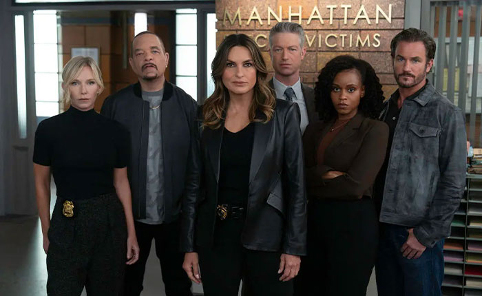 Group of serious detectives standing inside Manhattan Crime Victims office focused on US Marshals manhunt for West Wing star Timothy Busfield.
