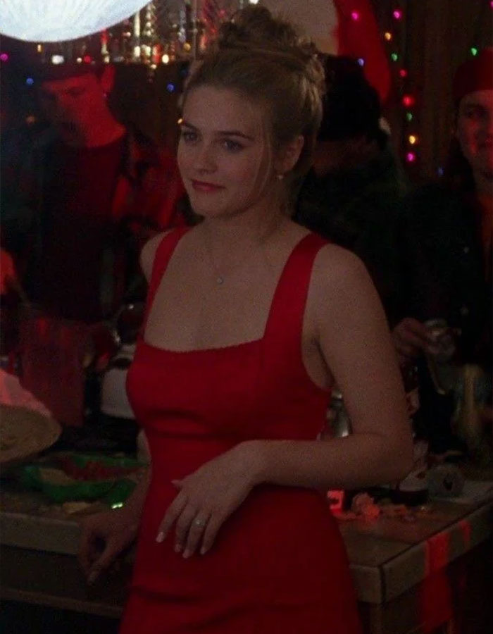 Alicia Silverstone in a red dress at a party, with background lights and people socializing indoors.