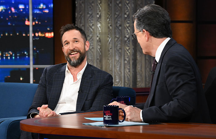 Noah Wyle smiling and talking on a late-night talk show, discussing his role and future in The Pitt season 2.