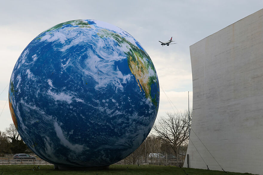 Large Earth model outdoors with an airplane flying overhead, illustrating concepts of planet value and Earth costs. Large Earth model outdoors with an airplane flying overhead, illustrating concepts of planet value and Earth costs.