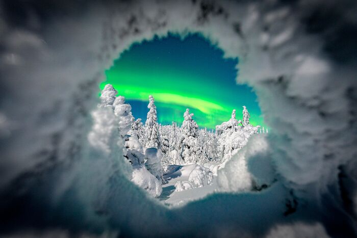 View of snowy winter forest and northern lights through a frosty tunnel, cozy images of winter to enjoy indoors.