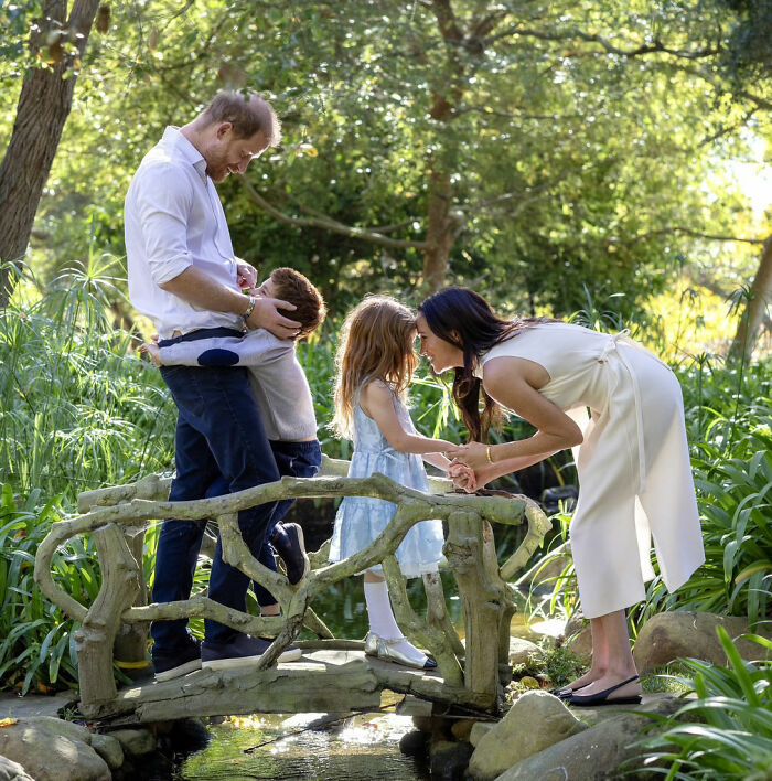 A family spending time outdoors on a small wooden bridge surrounded by greenery, highlighting Meghan Markle's 2016 throwback.