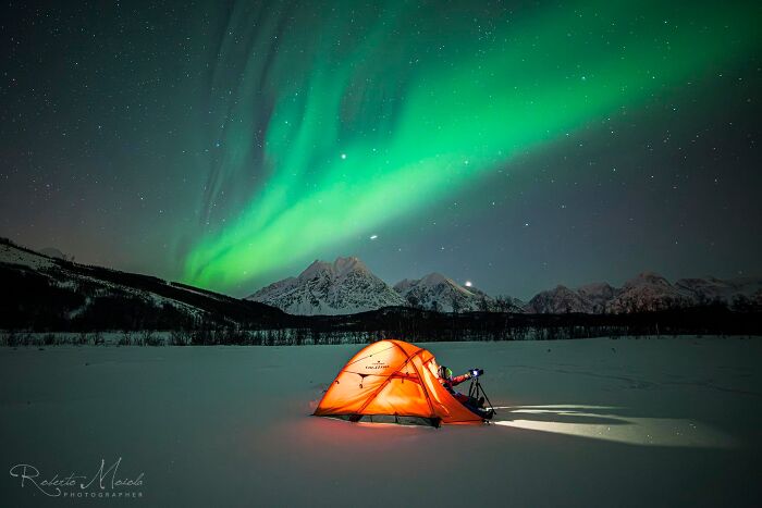 Glowing orange tent in snowy landscape under vibrant northern lights showcasing cozy winter outdoor scene.