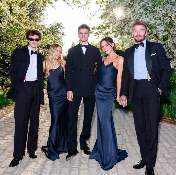 Brooklyn Beckham with parents David and Victoria Beckham and siblings dressed formally outdoors in a garden setting. Brooklyn Beckham with parents David and Victoria Beckham and siblings dressed formally outdoors in a garden setting.