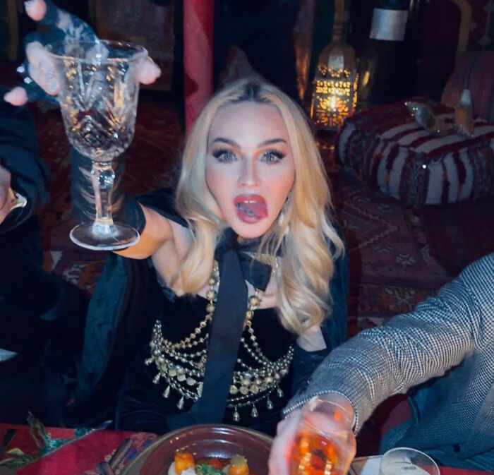 Madonna raising a glass in a Dolce & Gabbana ad featuring younger men with provocative styling and bold imagery. Madonna raising a glass in a Dolce & Gabbana ad featuring younger men with provocative styling and bold imagery.