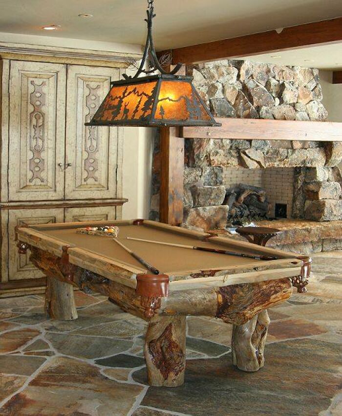 Rustic billiard table with beautifully crafted woodworking projects in a cozy room featuring stone fireplace and wooden beams.