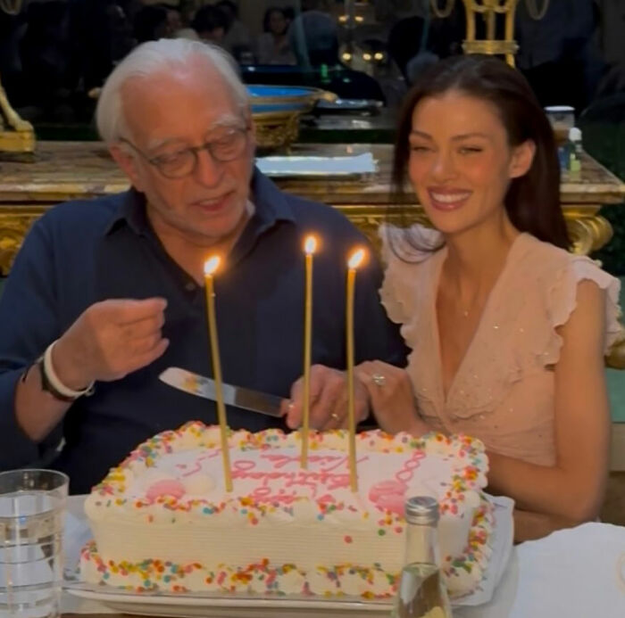 Older man and young woman smiling together behind a birthday cake, Nicola Peltz's background sparks theories. Older man and young woman smiling together behind a birthday cake, Nicola Peltz's background sparks theories.