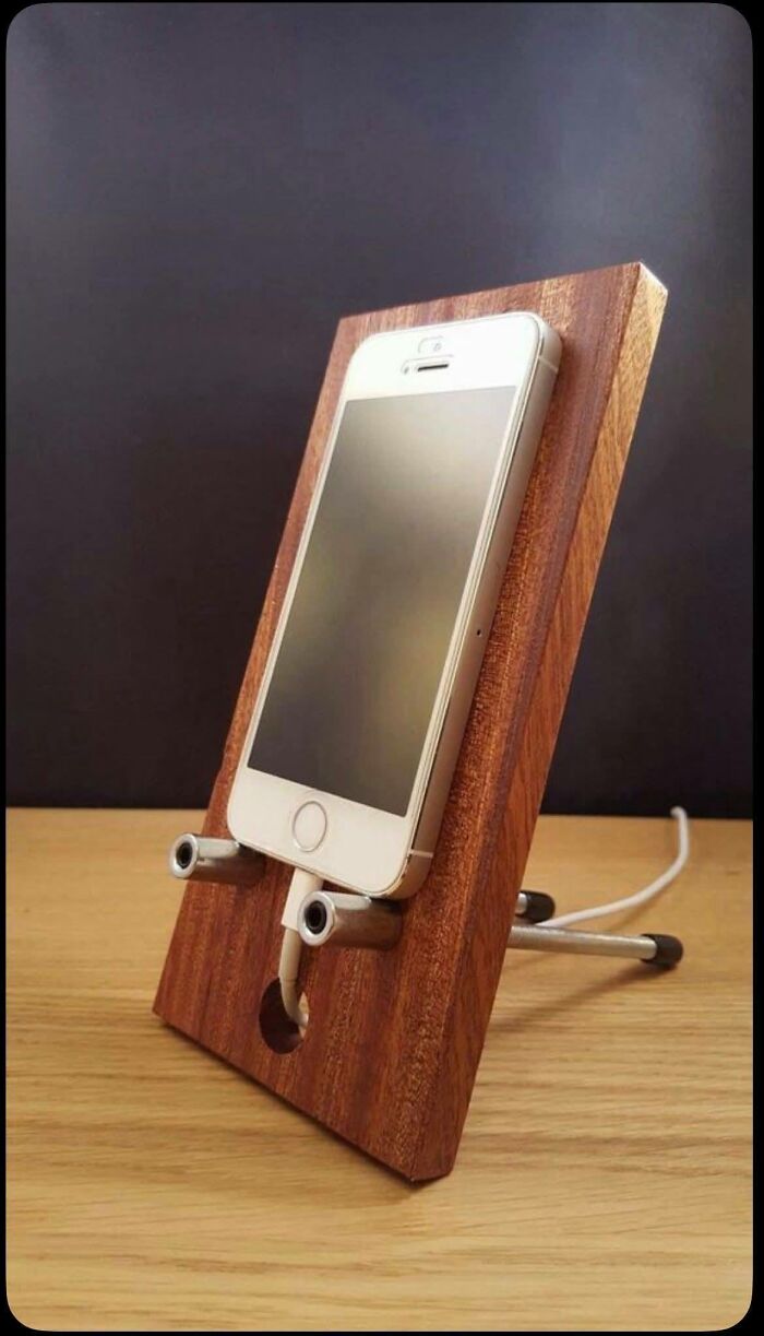 Wooden phone stand crafted with metal accents holding a smartphone, showcasing a beautifully crafted woodworking project.