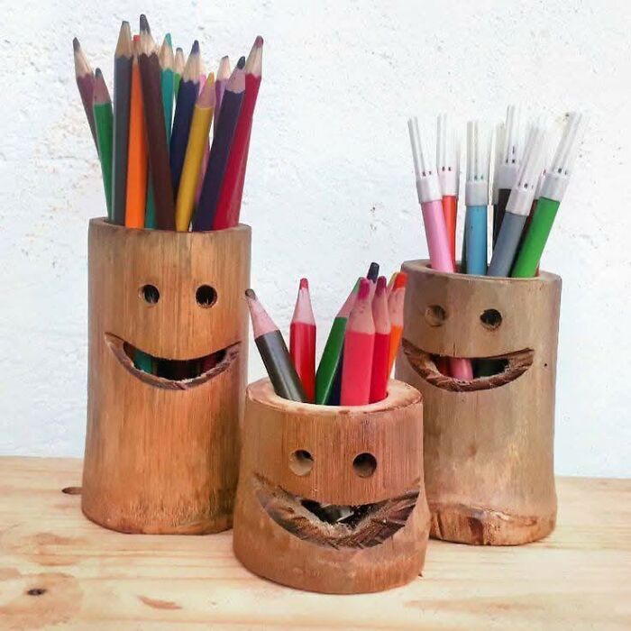 Three creatively carved wooden pencil holders with smiling faces, showcasing beautifully crafted woodworking projects with color pencils and pens.
