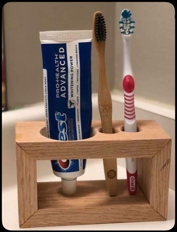 Woodworking project of a wooden toothbrush and toothpaste holder with bamboo and plastic toothbrushes on a bathroom counter.