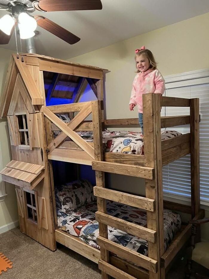 Child standing on a beautifully crafted wooden bunk bed designed like a playhouse, showcasing impressive woodworking projects.