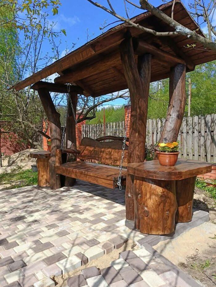 Rustic wooden swing with natural log design and roof in a garden setting showcasing woodworking projects outdoors.
