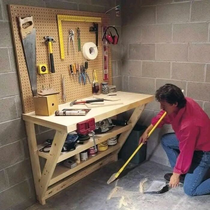 Man cleaning a workshop floor near a beautifully crafted woodworking projects bench with tools organized on pegboard.
