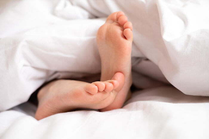 Bare feet sticking out from under white bed sheets, capturing a relatable moment that hits people harder than expected.