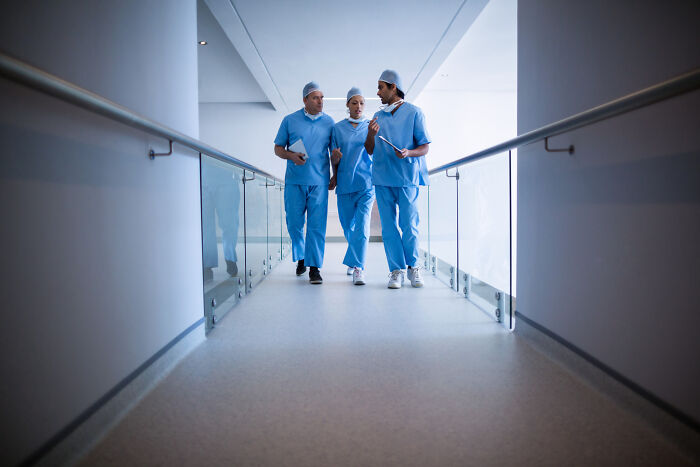 Three doctors in blue scrubs walking and discussing patient care in a hospital corridor, illustrating unethical behavior risks.