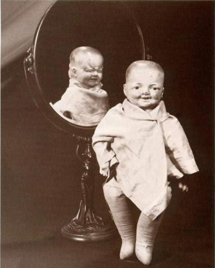 Vintage creepy doll with an eerie face reflected differently in an old black and white photo, highlighting odd and creepy vibes.
