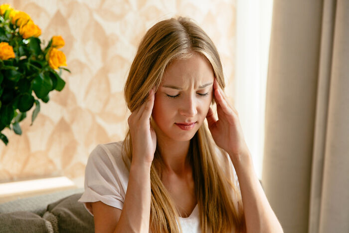 Young woman holding her head in pain at home, experiencing moments that hit people harder than expected.