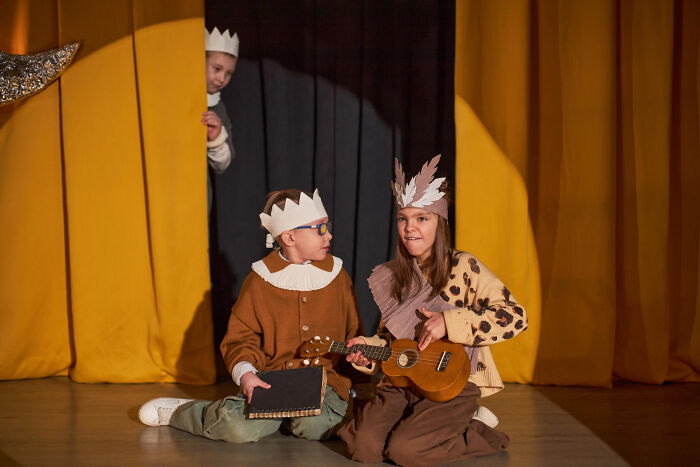 Children in costumes playing musical instruments on stage, capturing iconic and satisfying moments with a not my problem attitude.