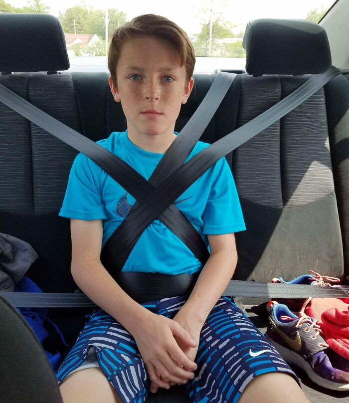 Boy sitting in car backseat with seatbelts wrapped around him, illustrating fun moments with siblings.