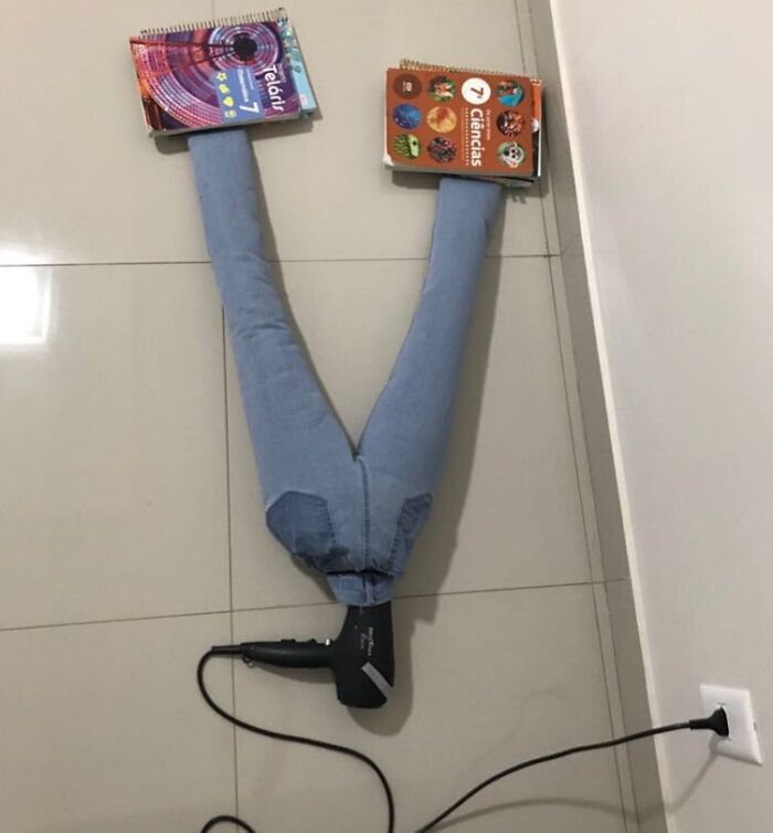 Creative sibling fun with jeans, books, and a hairdryer arranged to mimic legs on a tiled floor.