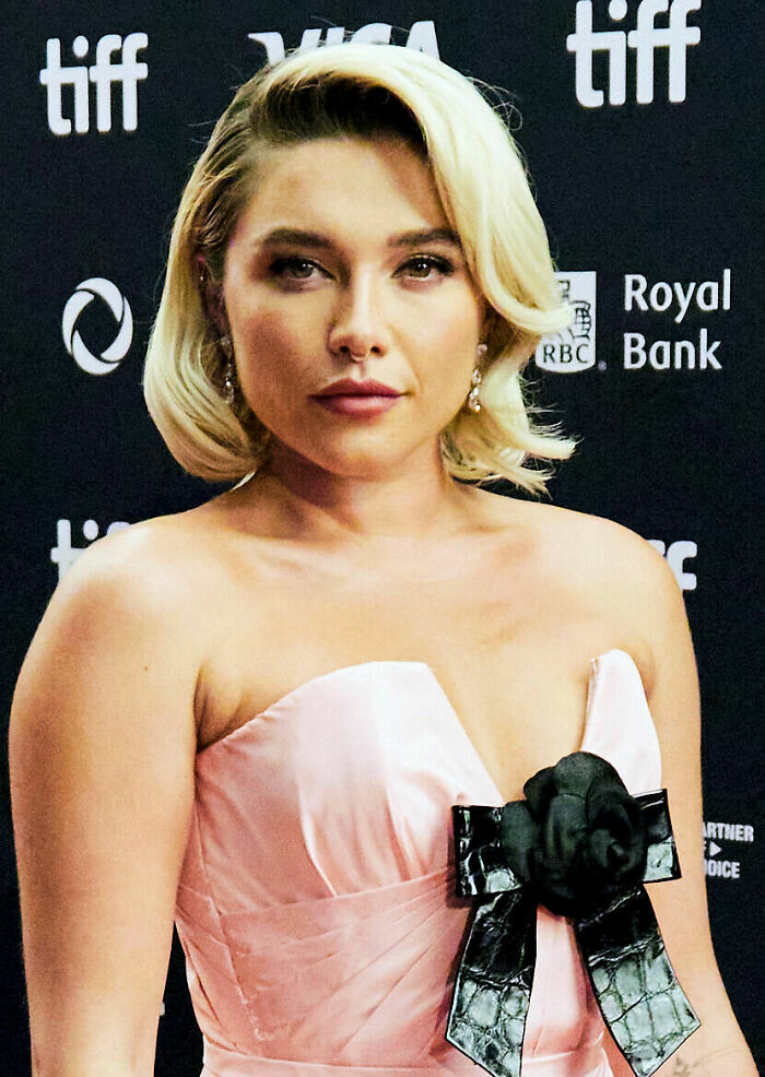 Florence Pugh at a film festival event, wearing a pink dress with a black bow, showcasing her bio and career highlights.