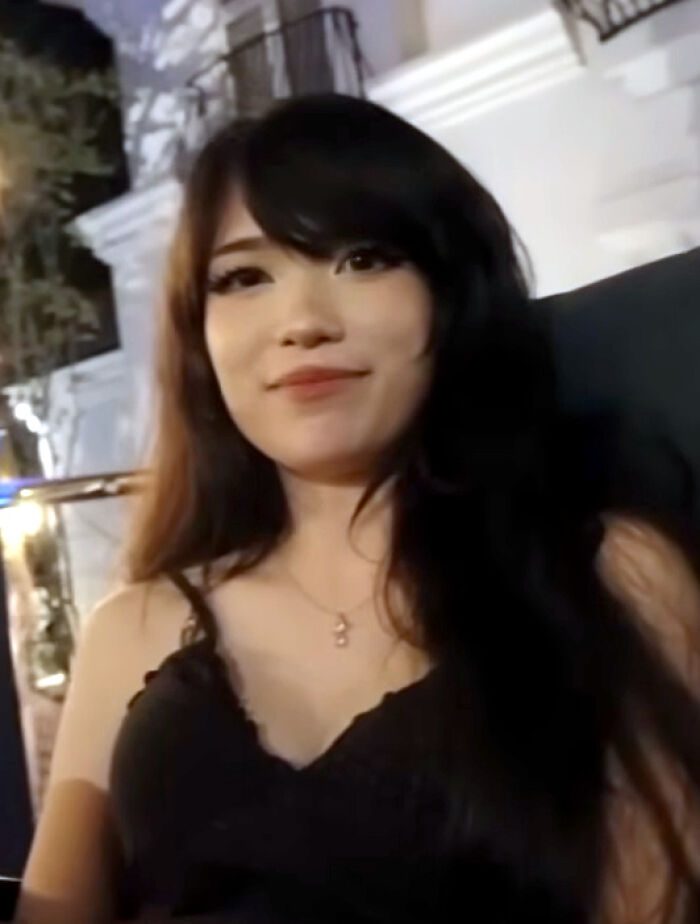 Emiru smiling outdoors at night, wearing a black top with long dark hair, showcasing her bio and career highlights.