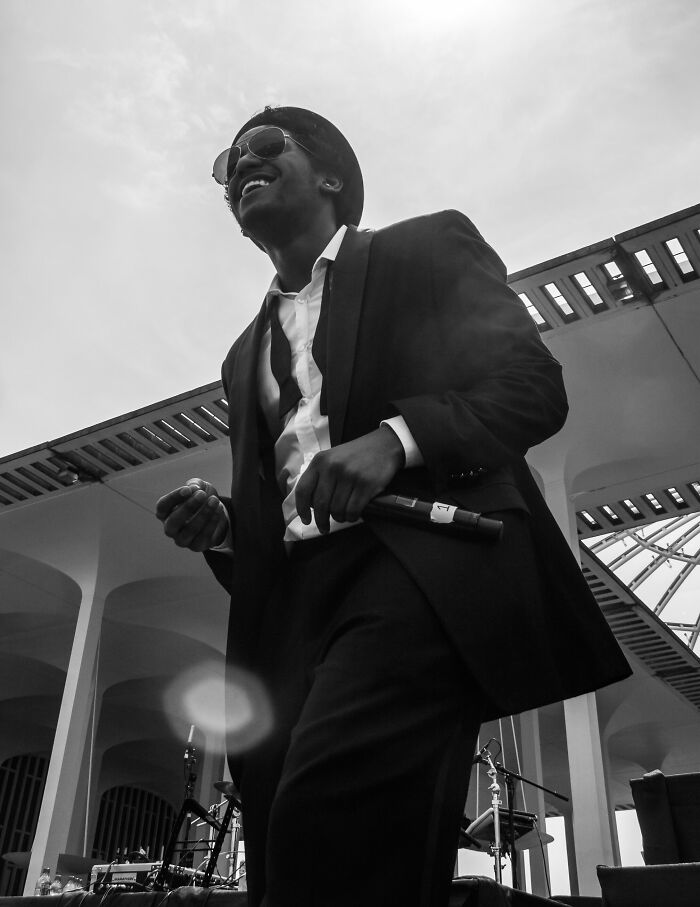 Lloyd performing on stage wearing sunglasses and a suit during a live music event in an outdoor venue.