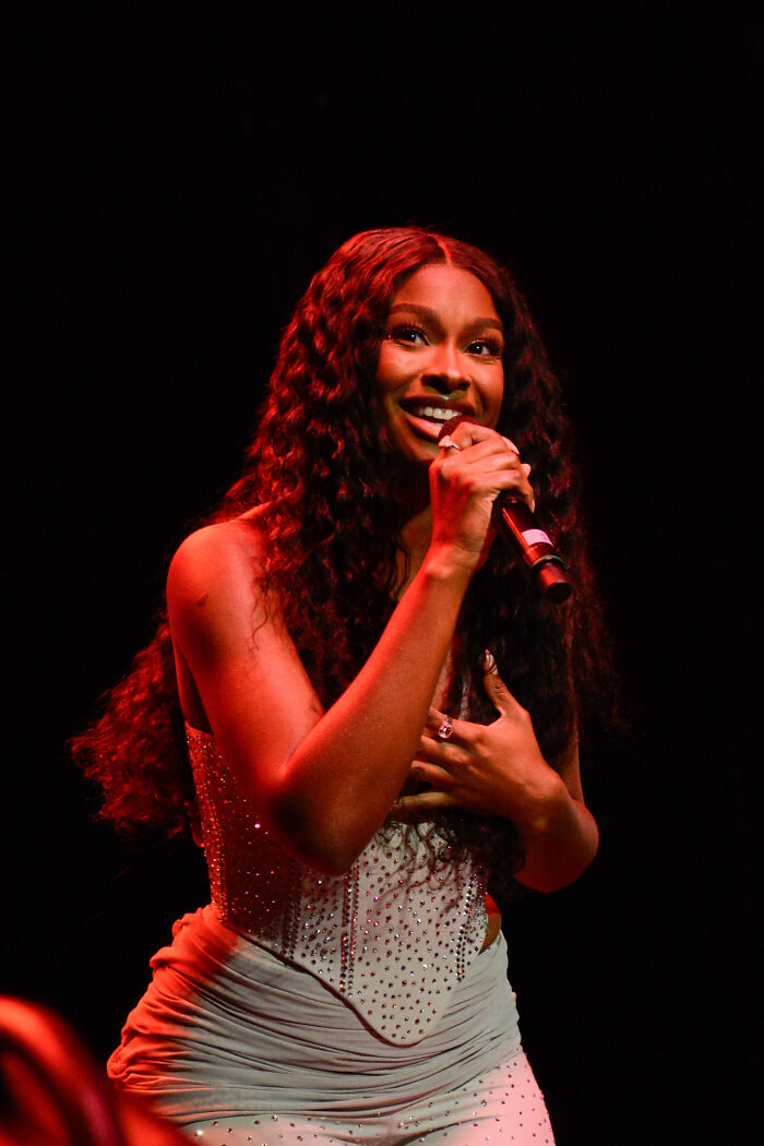 Coco Jones performing on stage with microphone, smiling and wearing a sparkling outfit in a live music event.