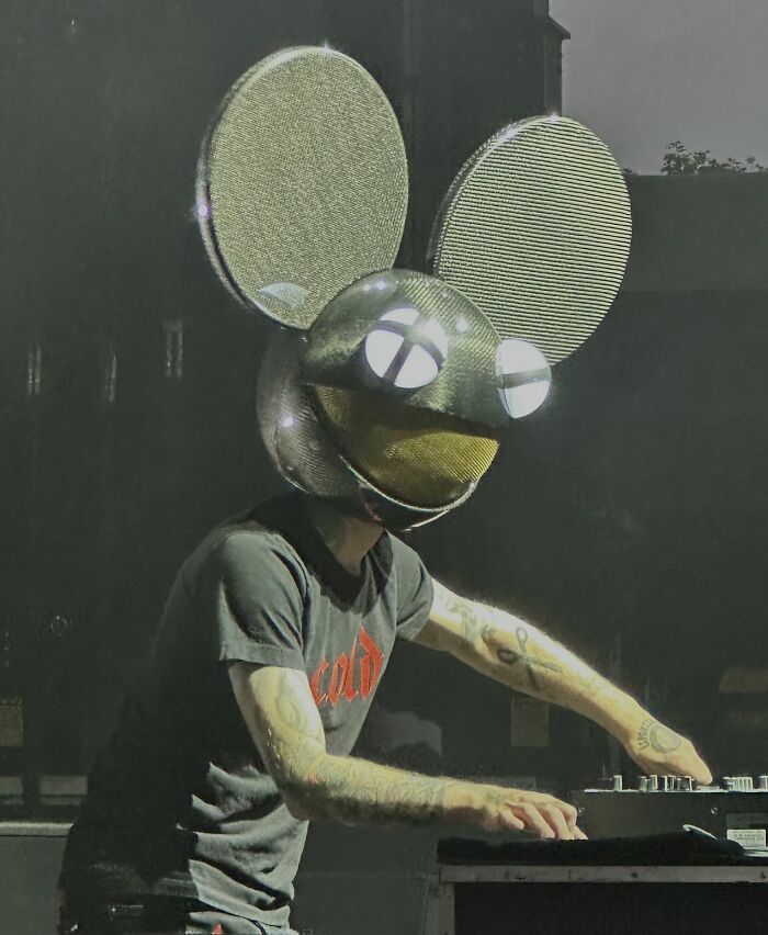 Deadmau5 performing live wearing signature mouse helmet and mixing music on stage in a dark setting.
