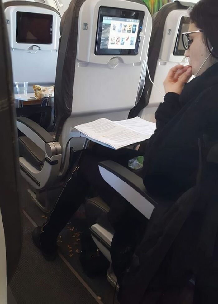 Woman on airplane with feet up, papers on tray and snack shells scattered on floor, example of next-level jerks