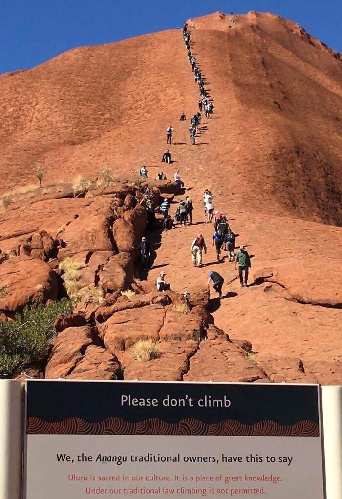 Crowd of tourists climbing Uluru past a please don't climb sign, next-level jerks