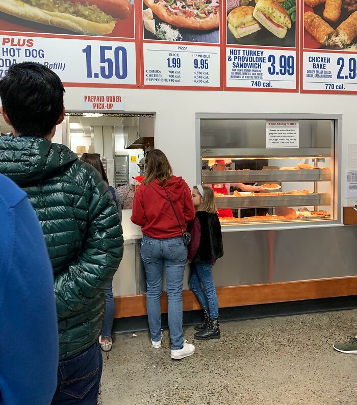 Customers at a food court pizza counter with a family at the pickup window, others crowding the queue — next-level jerks