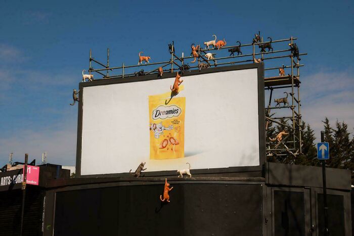 Billboard print advertisement for Dreamies cat treats with creative cat figurines climbing and interacting with the display.