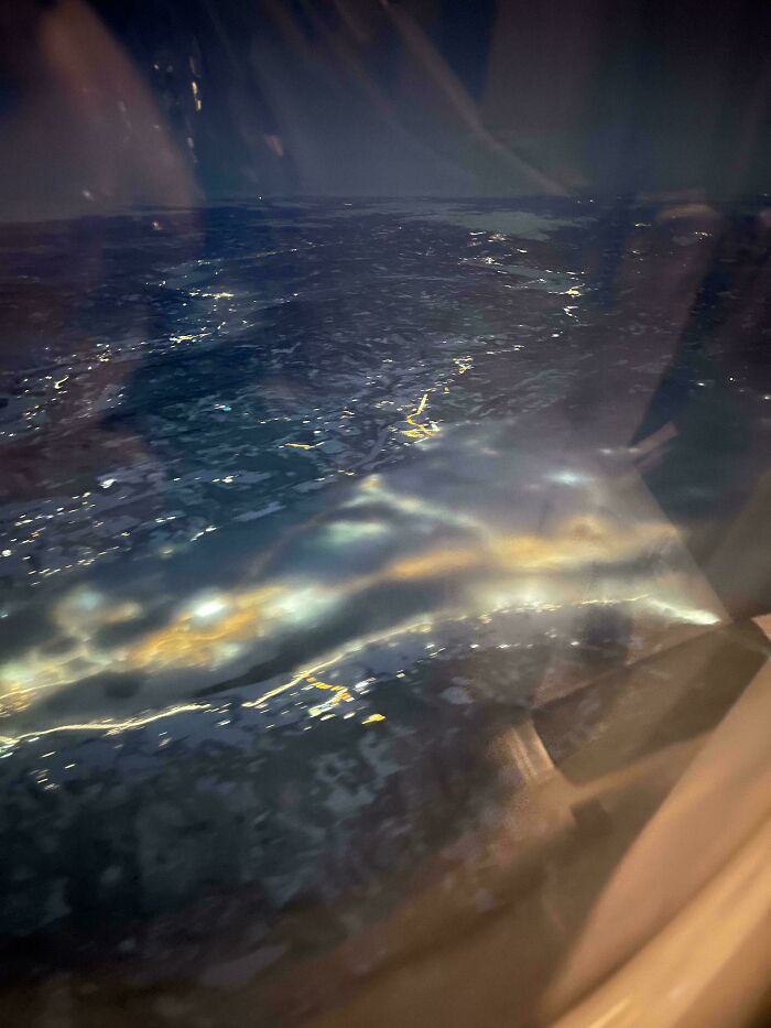 Night aerial view through airplane window showing blurred city lights and glowing streaks, glitches in the matrix.