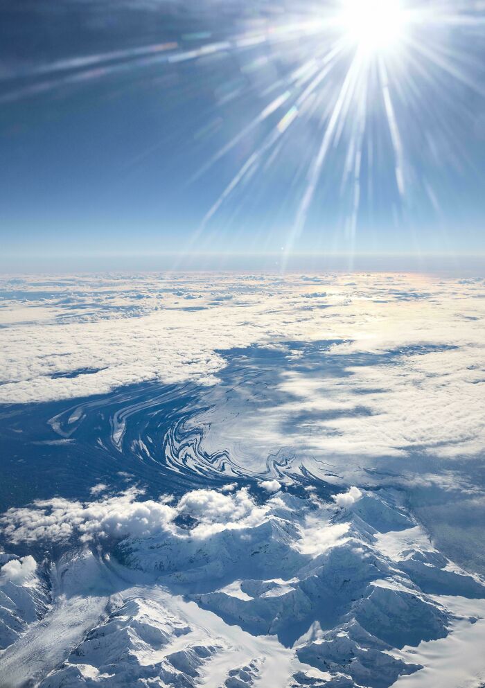 Aerial view of snow-capped mountains, swirling ocean patterns and bright sun rays suggestive of glitches in the matrix