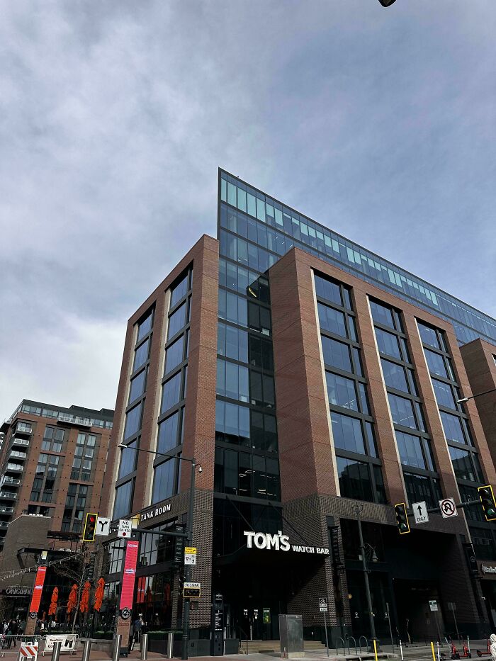 Corner glass and brick office building with Tom's Watch Bar signage, city street under overcast sky, glitches in the matrix