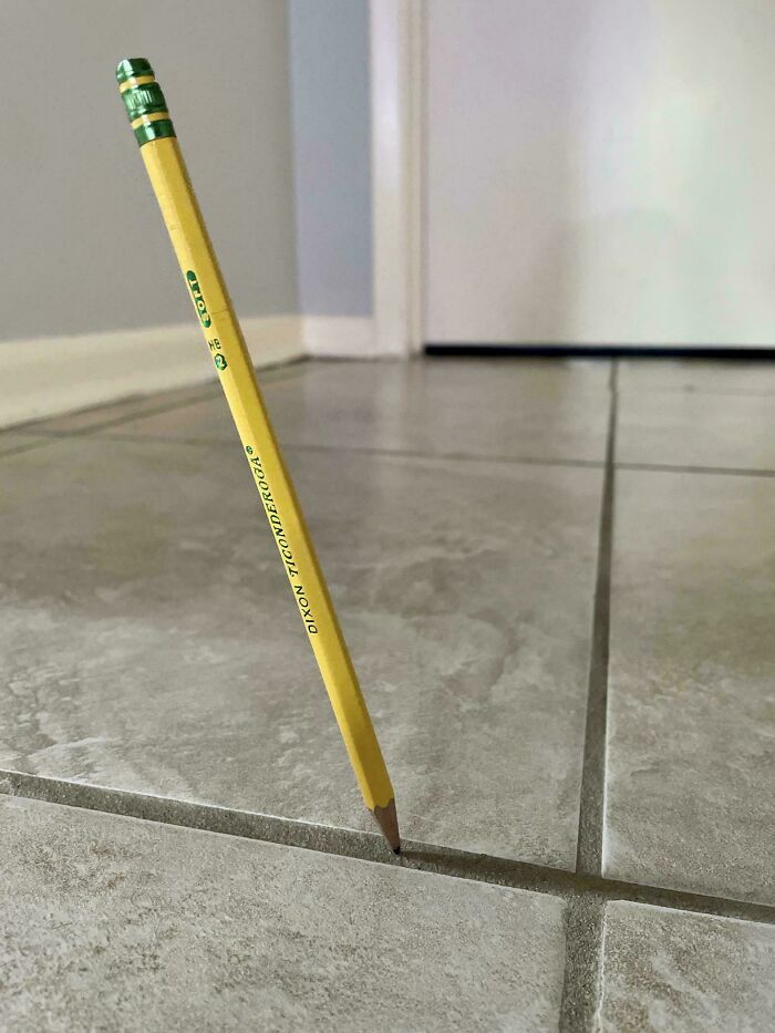 Pencil balanced upright on tile grout line, a real-life glitch in the matrix.
