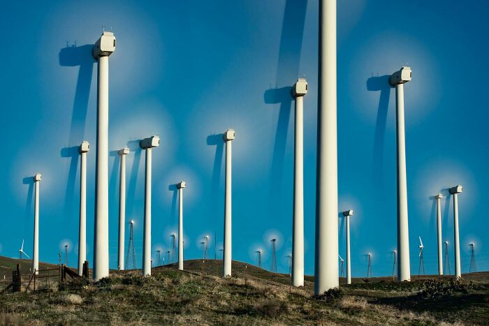 Wind turbines on rolling hills with blurred spinning halos, surreal glitches in the matrix visual effect.